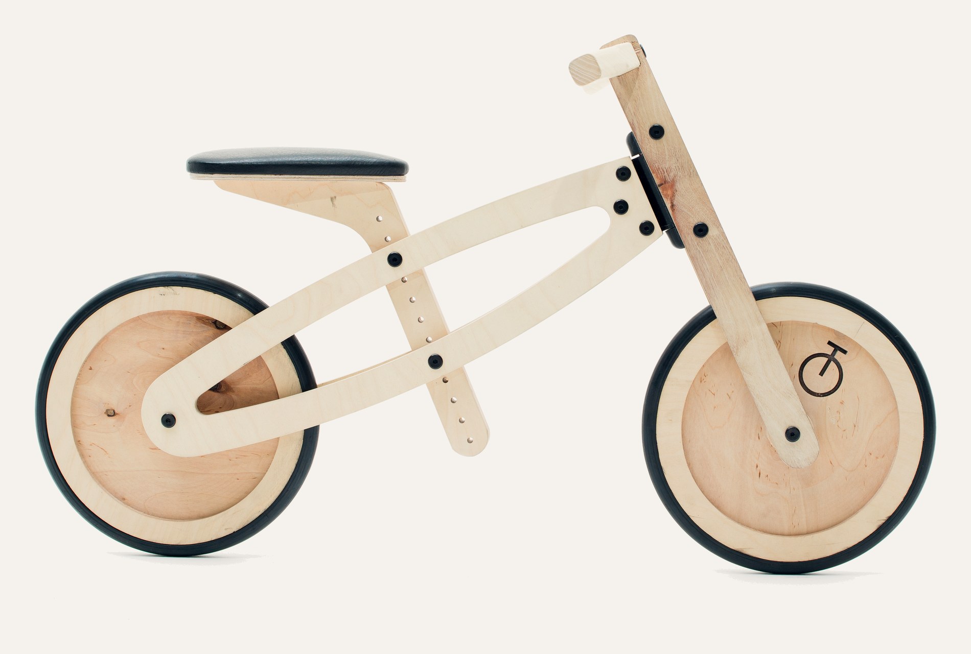 A Tochak balance bike photographed from the side: birch plywood frame, natural wheels, leather seat.