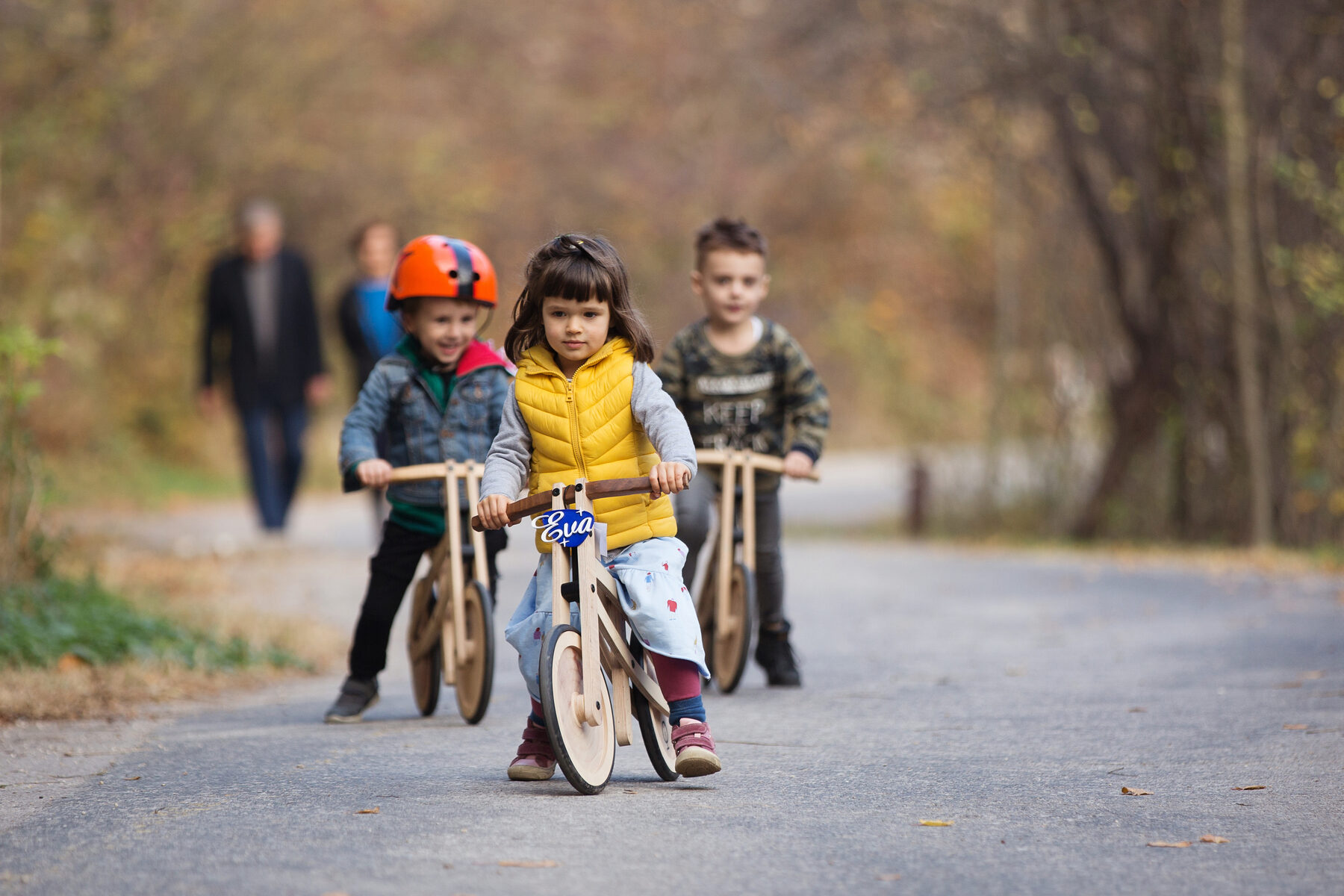Three children ride natural, unpainted Tochaks side by side along a paved road in autumn.